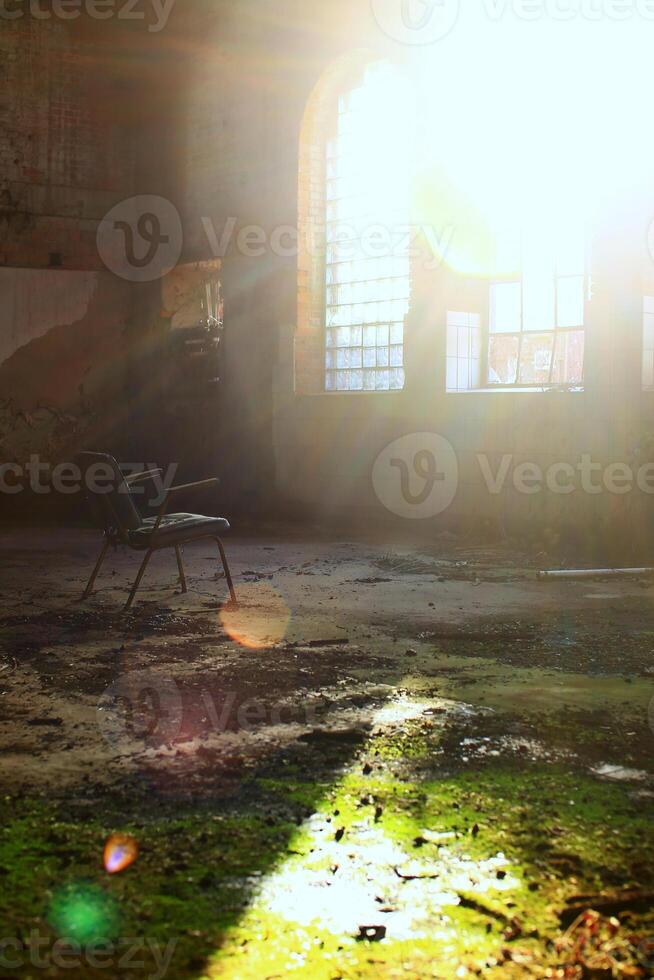 Spooky shot of chair in overgrown abandoned factory interior in backlight with flares photo