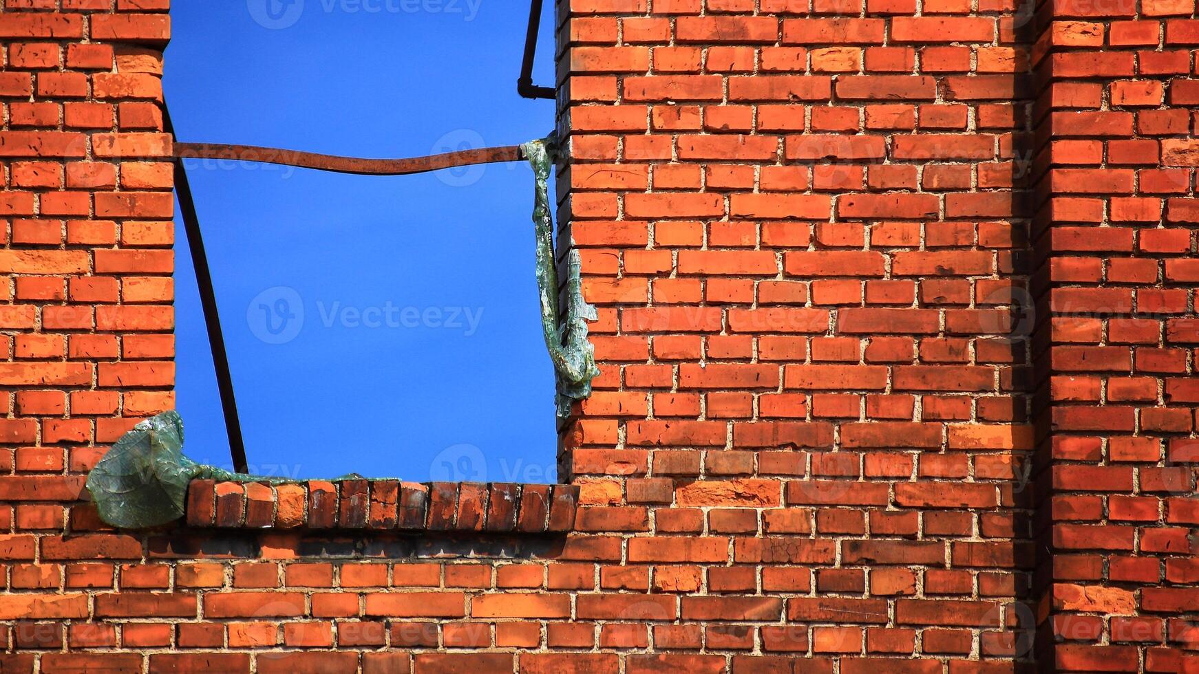 Window frame in brickwall with blue sky, the glass is molten due to a heavy fire photo