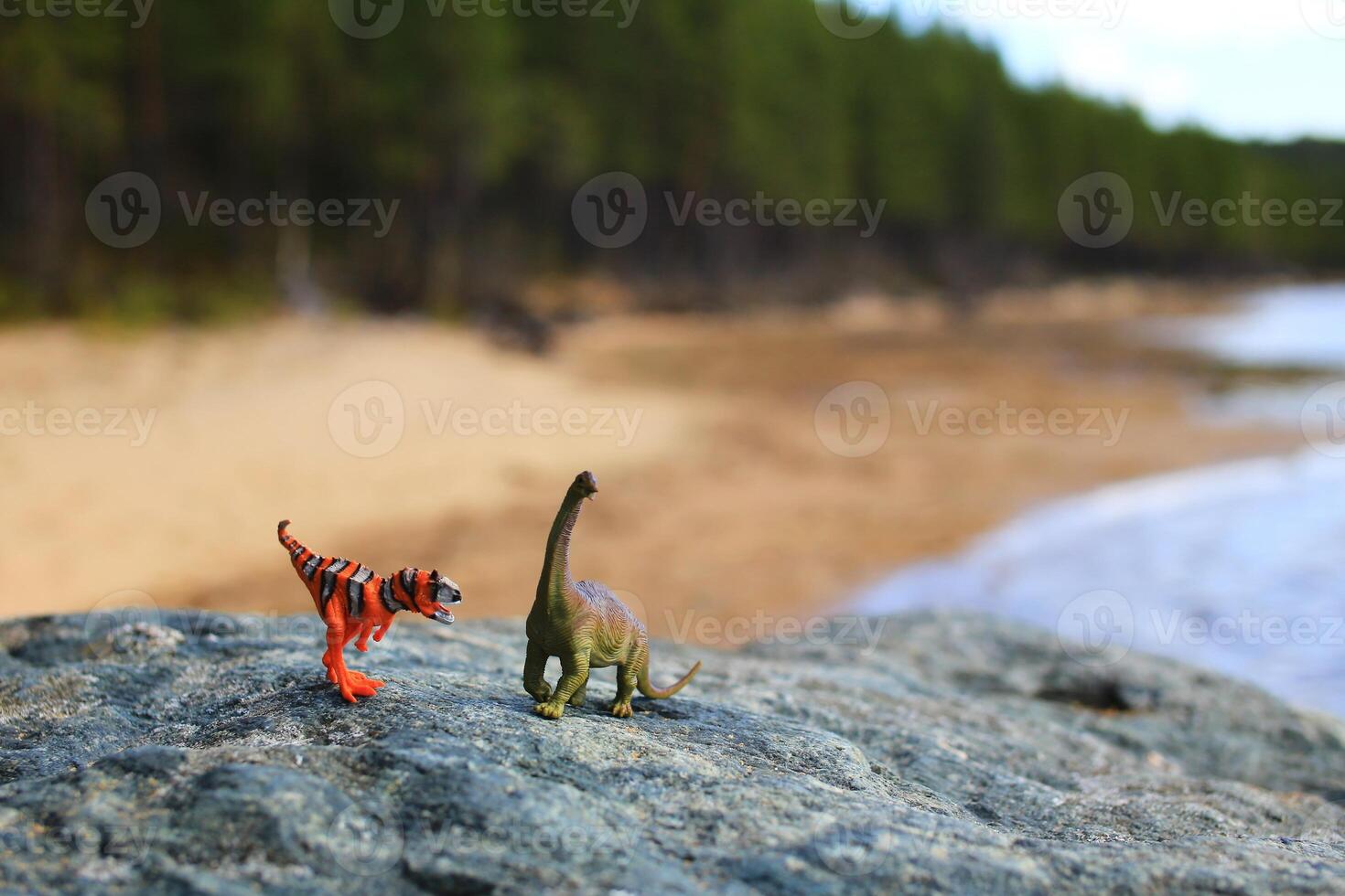 Two toy dinosaurs on a boulder at the beach photo