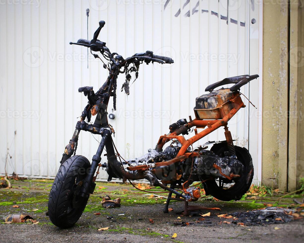 Burnt and charred remains of a moped in front of garage door photo