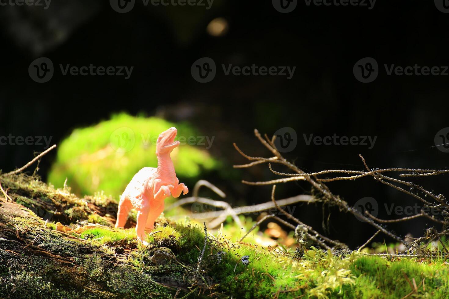 Toy dinosaur on mossy log in forest scene in the sunlight photo