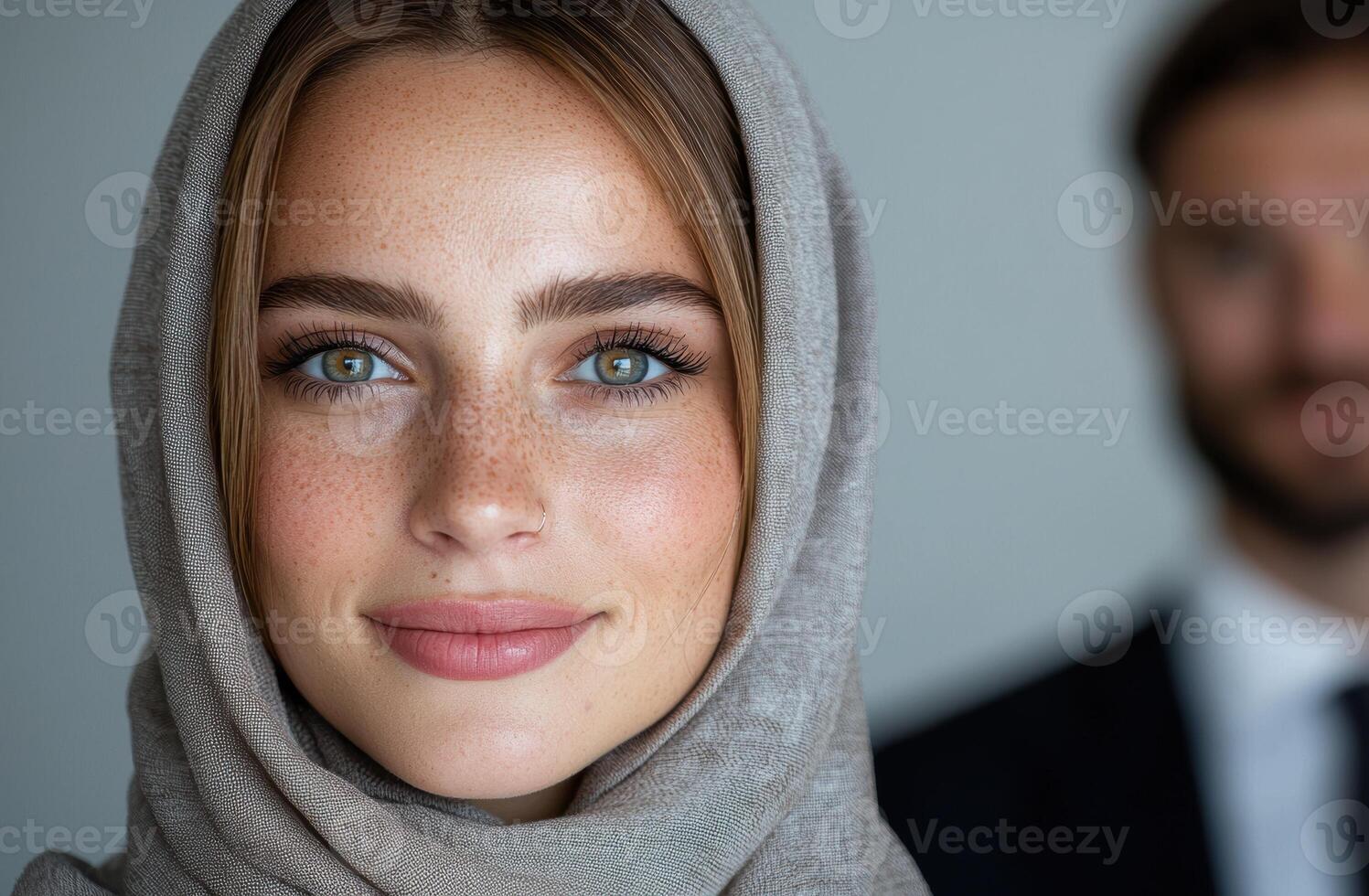 Close up portrait of a young woman wearing a hijab, with a blurred man in the background photo