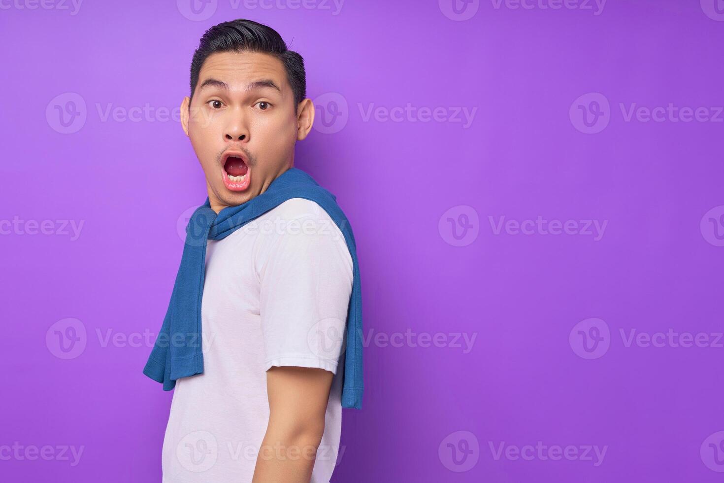 Surprised young Asian man wearing white t-shirt is standing and looking at camera isolated over purple background. people lifestyle concept photo