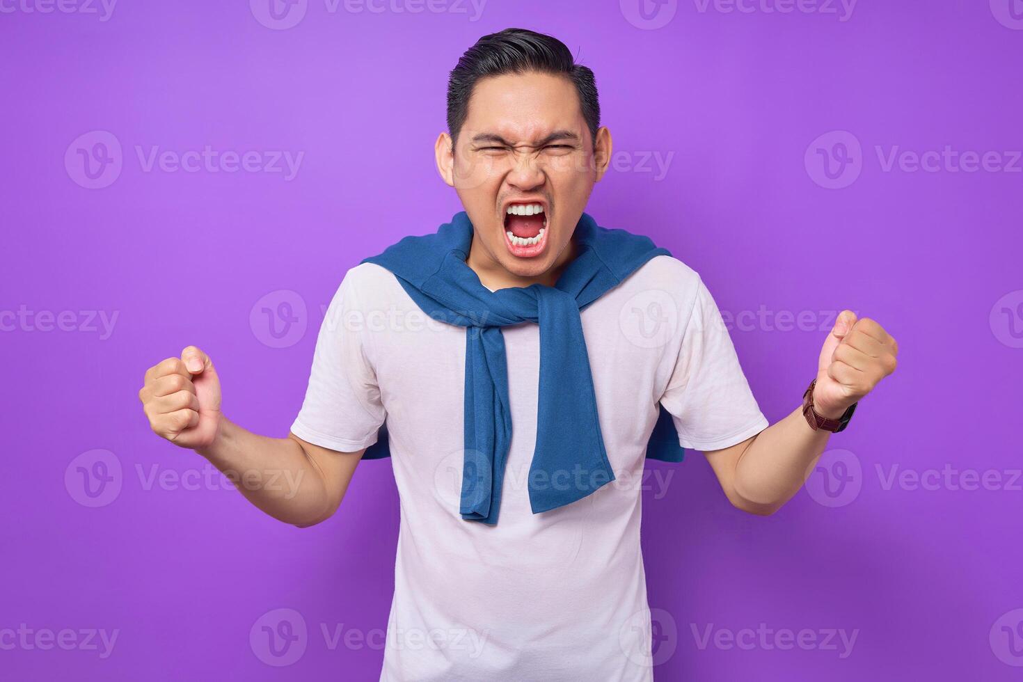 angry stressed young Asian man wearing white t-shirt spreading his hands screaming and shouting isolated over purple background. people lifestyle concept photo