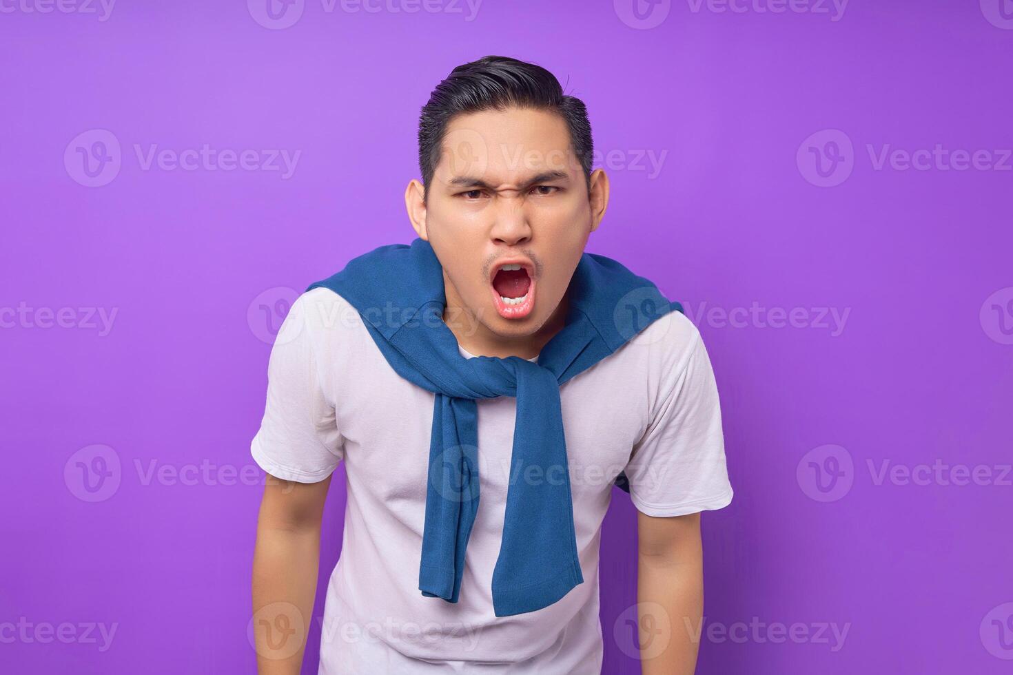 Surprised young Asian man wearing white t-shirt looks camera with opened mouth say wow isolated over purple background. people lifestyle concept photo