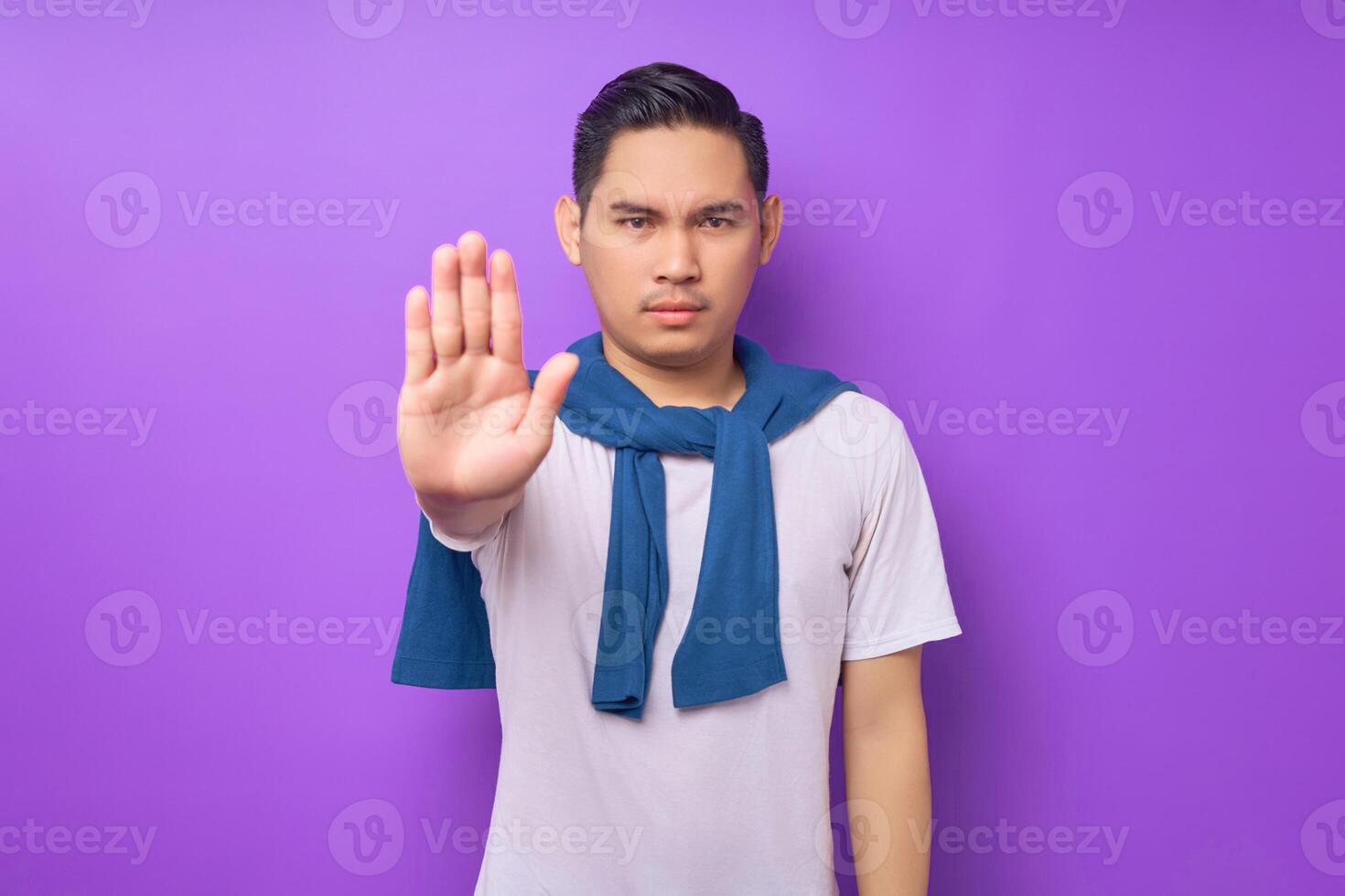 serious strict angry young Asian man wearing white t-shirt showing stop palm gesture refusing isolated over purple background. people lifestyle concept photo