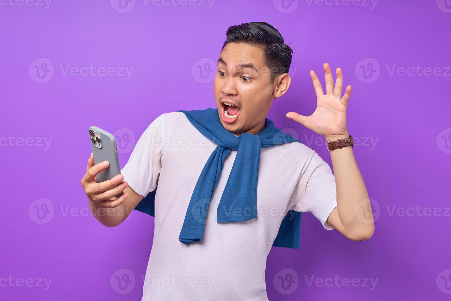 Surprised young Asian man using smartphone and reading special offer isolated over purple background photo