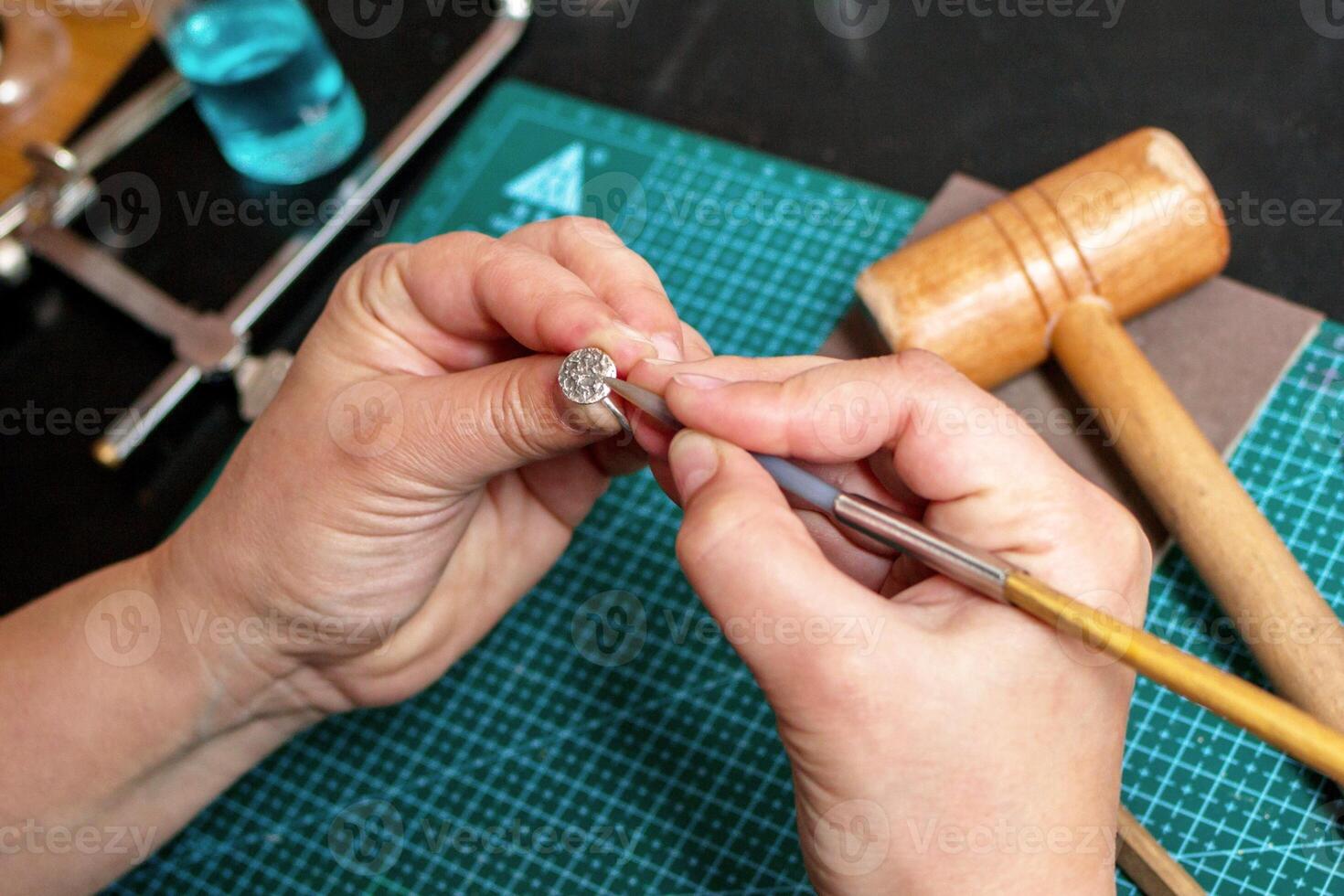 Woman-jeweler is working with silver ring on background of jewelry workplace and different tools. photo