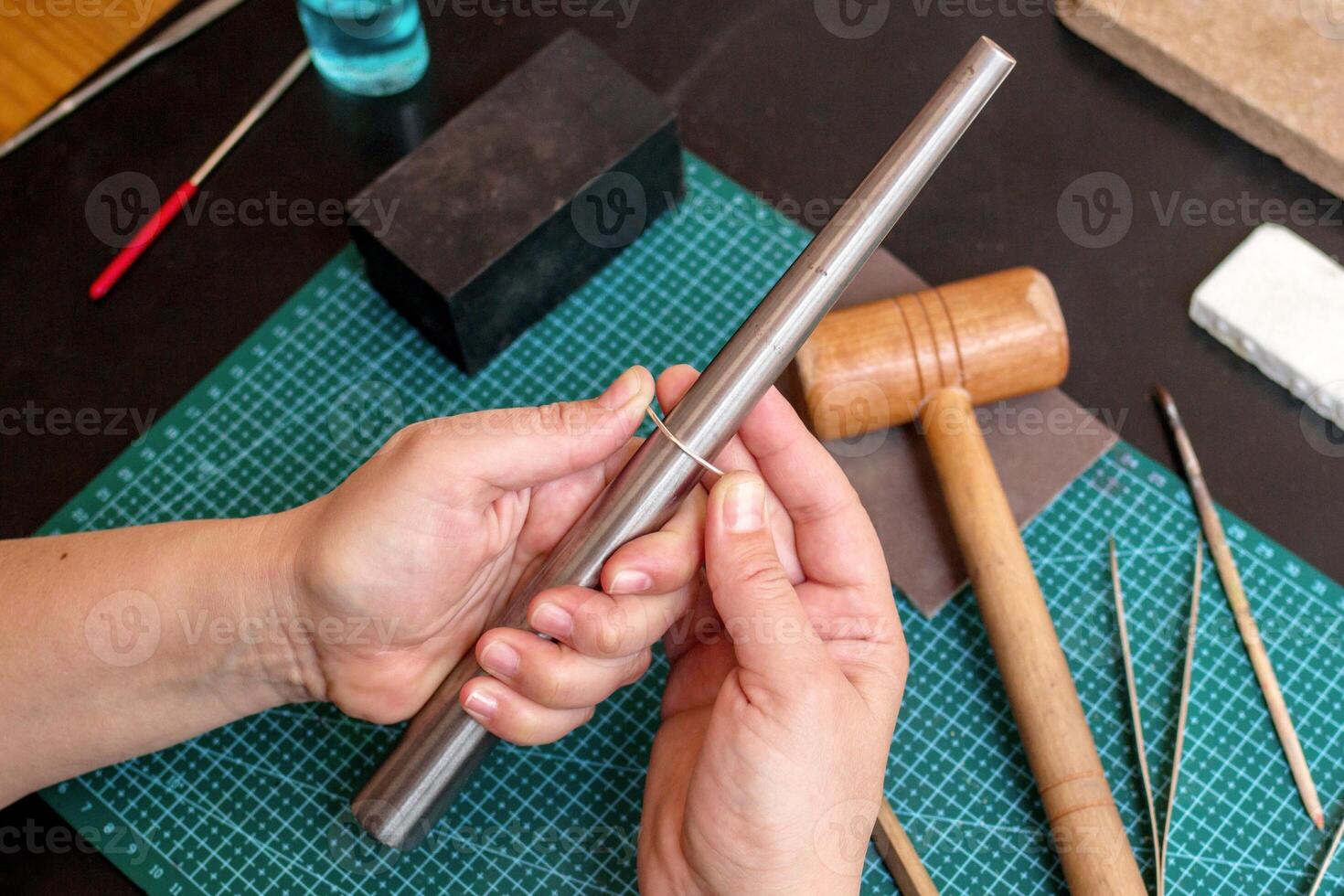 Female hands is carefully crafting a ring from a metal rod with a hammer on a green table. photo