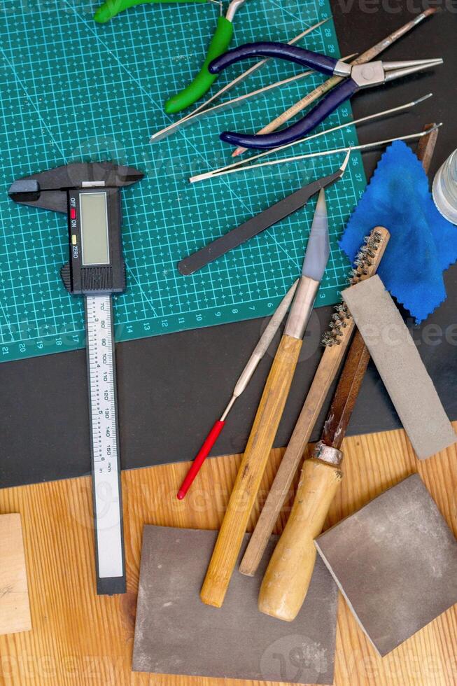 Variety of tools in an jewelry workplace on a green cutting mat - caliper, pliers, brushes. photo