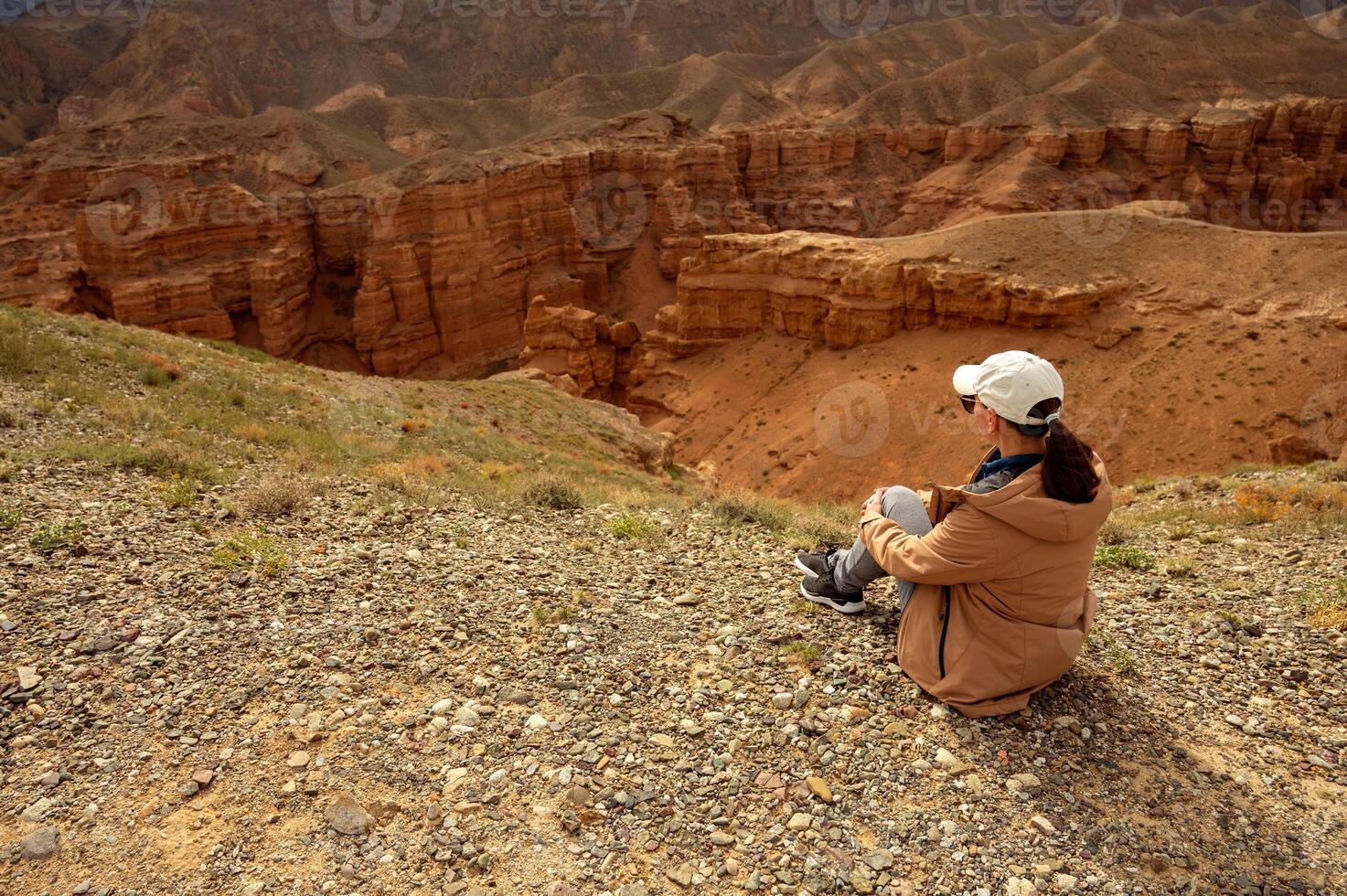 female tourist sits on a hill and looks at the beautiful orange canyon mountains and cloudy sky photo