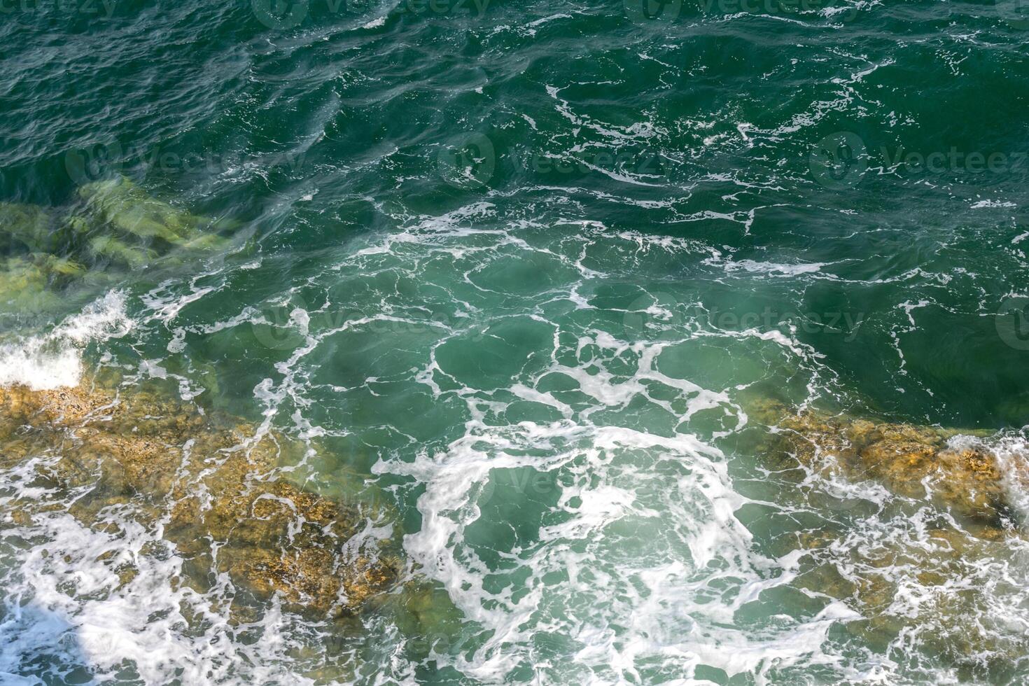 Sea waves crash against rocks and form foam photo