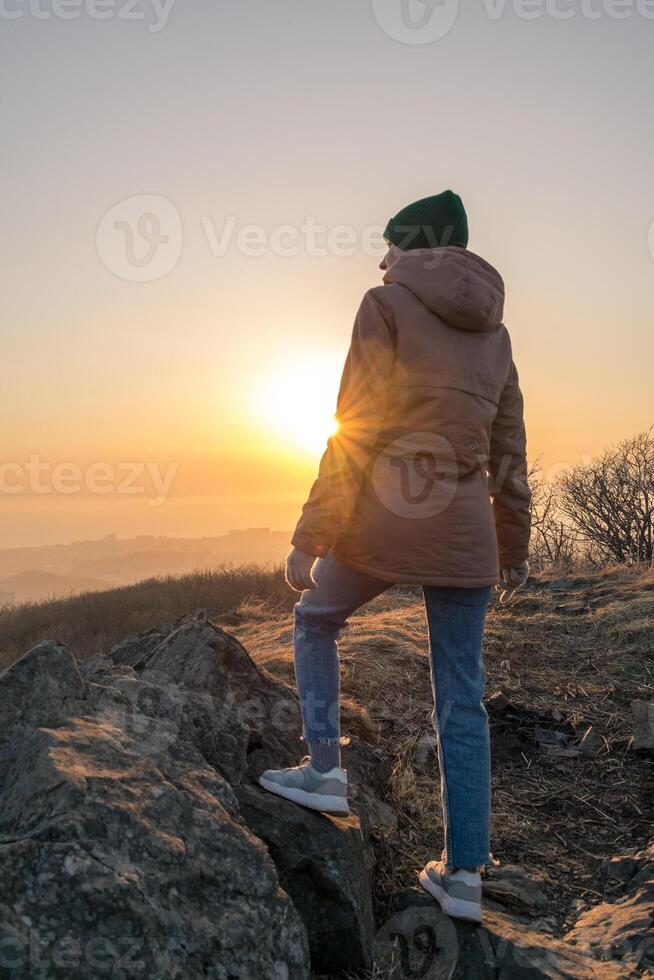 Girl in a jacket and a hat on the mountain during sunset photo