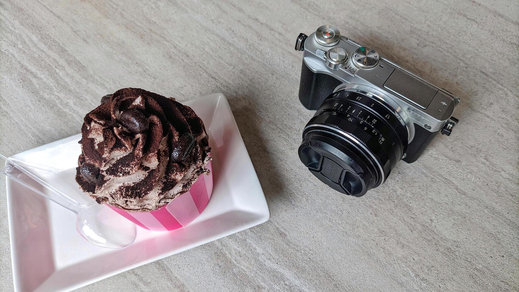 Mirrorless camera in retro style and cake or croissant on wooden table. photo
