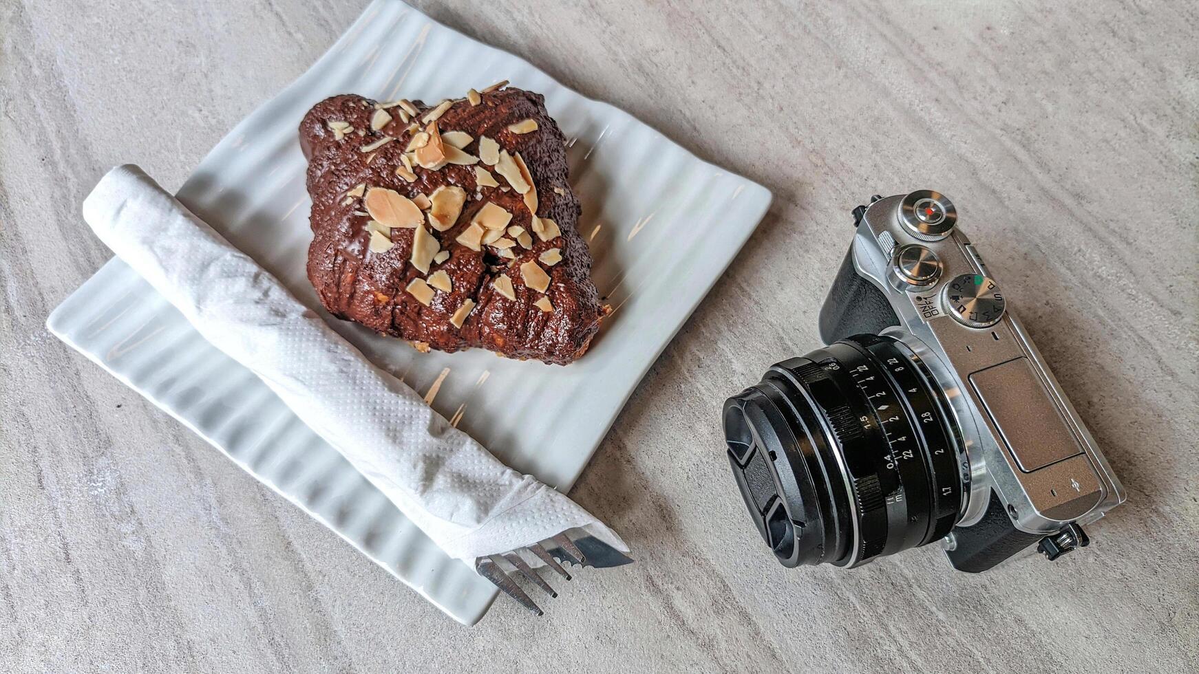 Mirrorless camera in retro style and cake or croissant on wooden table. photo