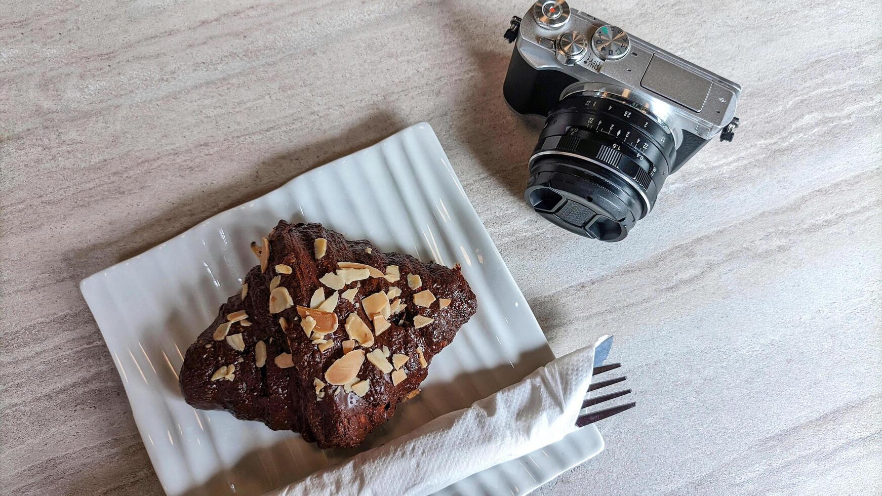 Mirrorless camera in retro style and cake or croissant on wooden table. photo