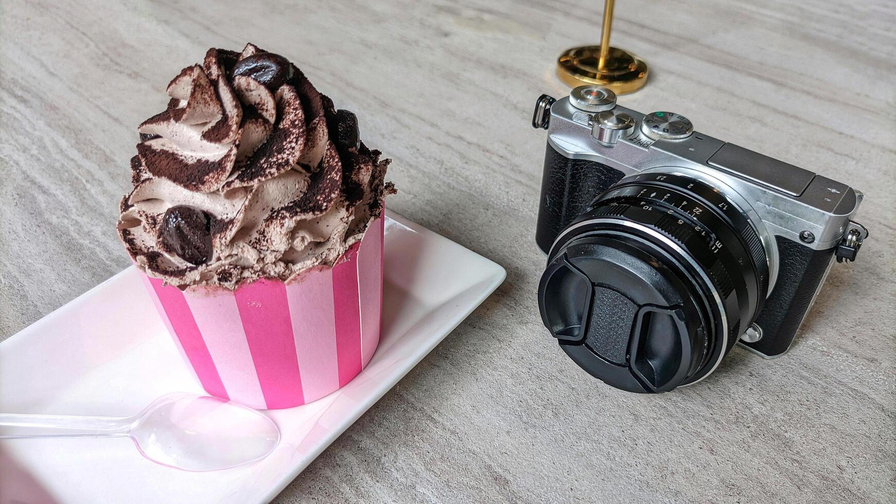 Mirrorless camera in retro style and cake or croissant on wooden table. photo