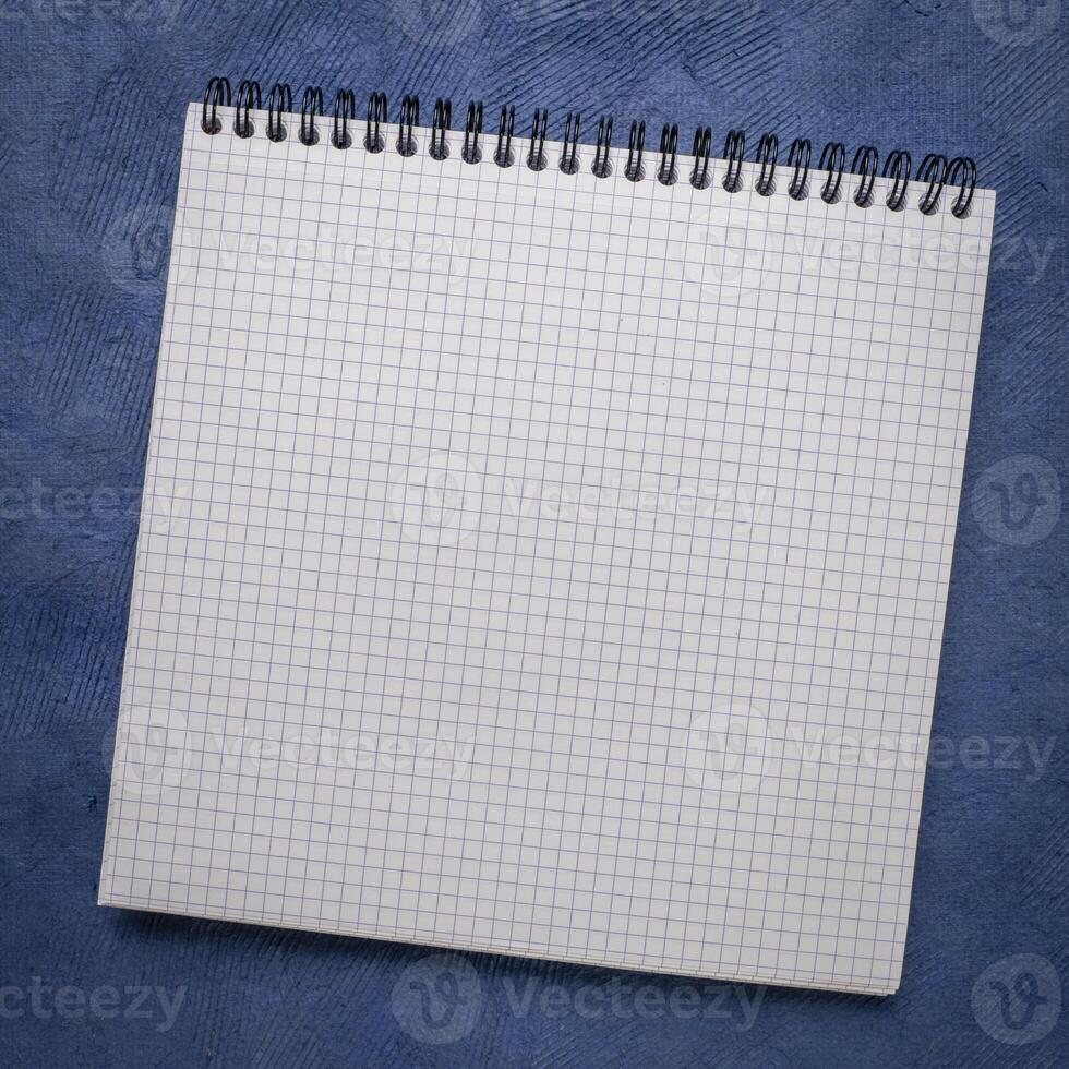 blank spiral notebook with grid paper on textured art paper photo