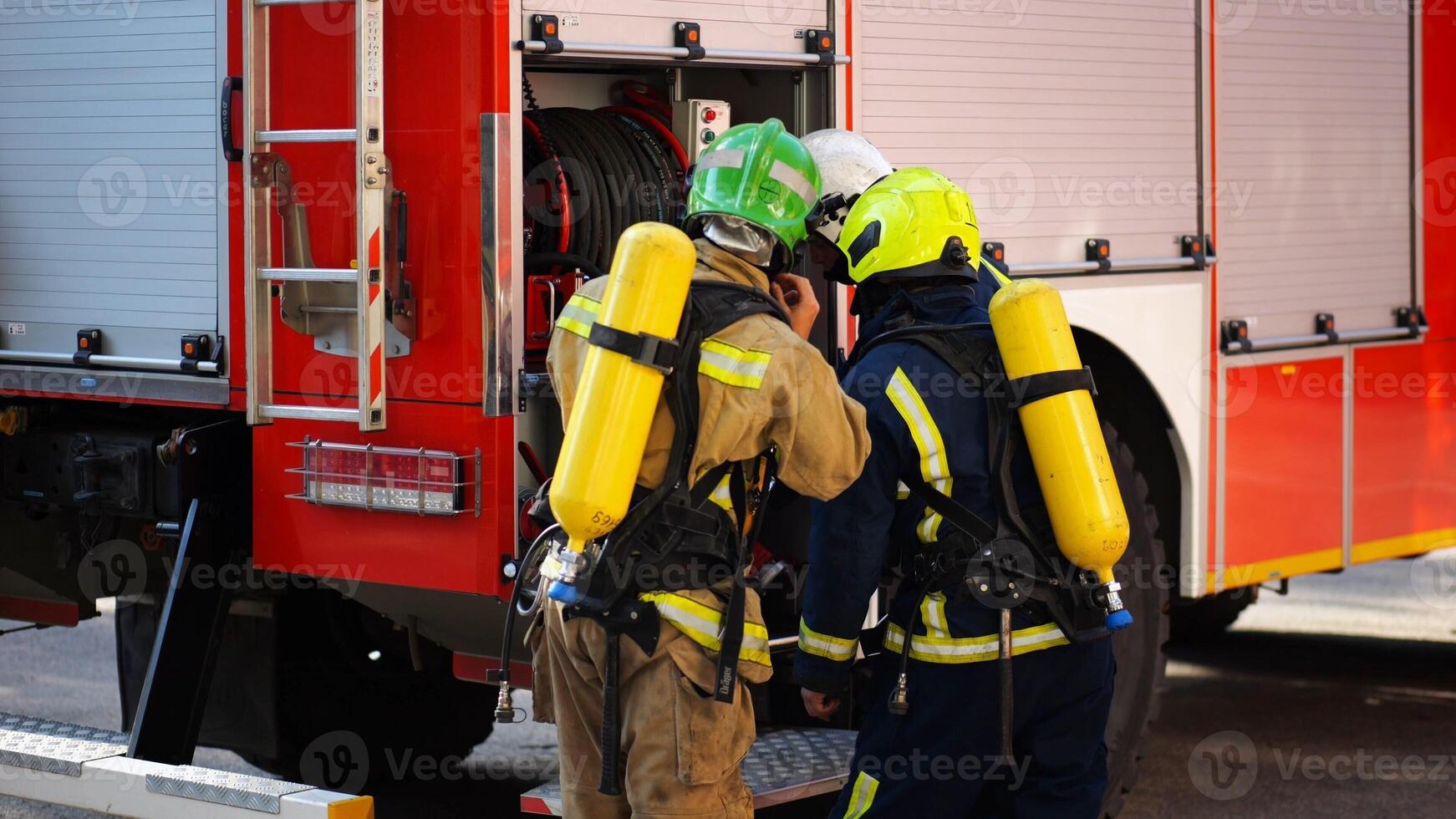 Young firemen prepare to extinguishing fire near big truck. Male firefighters in full equipment ready to putting out fire near a red car. Concept of saving lives and heroic profession. Slow motion photo