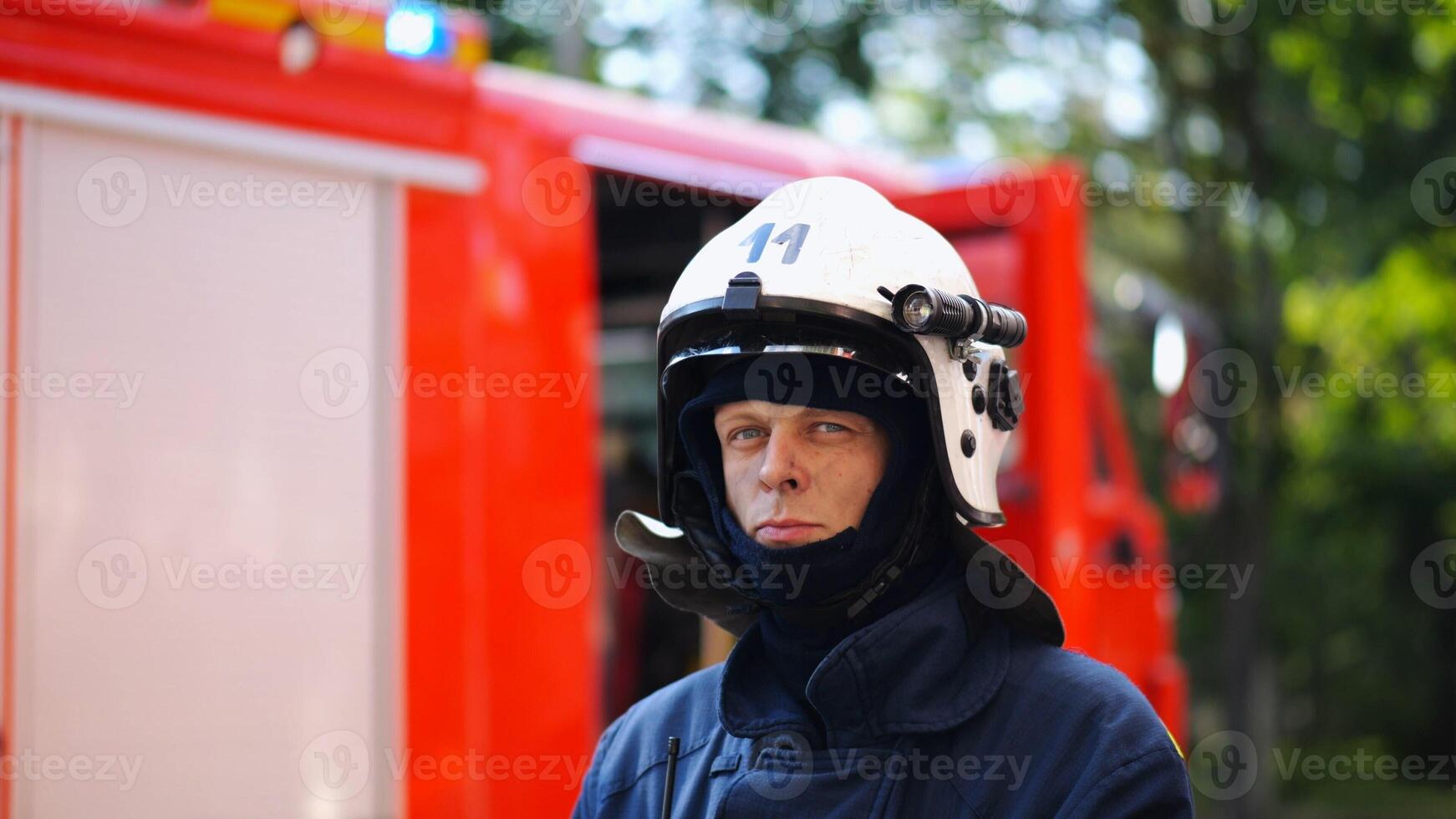 Portrait of confident male fireguard with dirty face standing near a fire engine. Young fireman in full equipment posing after fire against the background of big red truck. Concept of saving lives photo