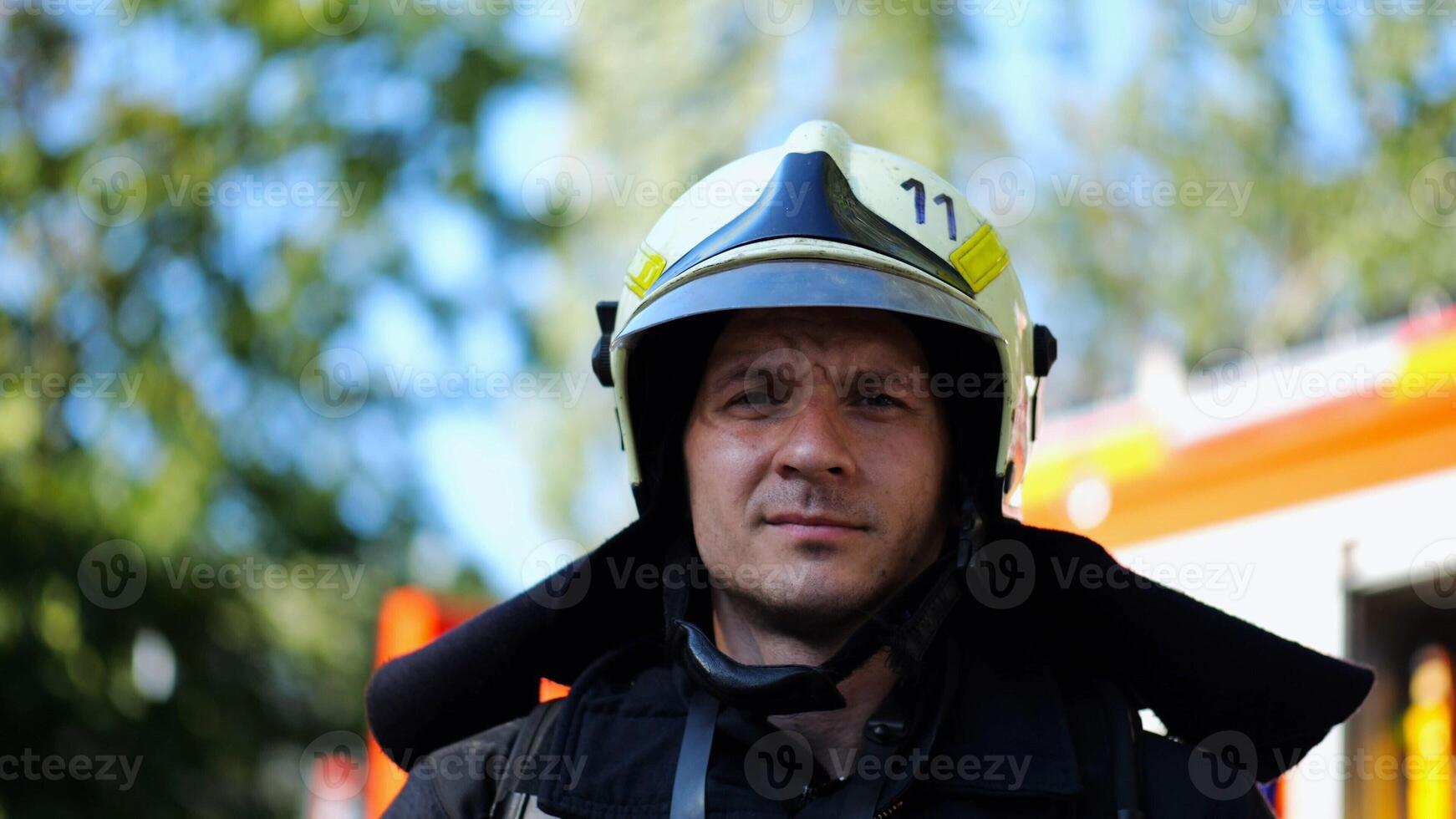 Portrait of confident male fireguard with dirty face standing near a fire engine. Young fireman in full equipment posing after fire against the background of big red truck. Concept of saving lives photo