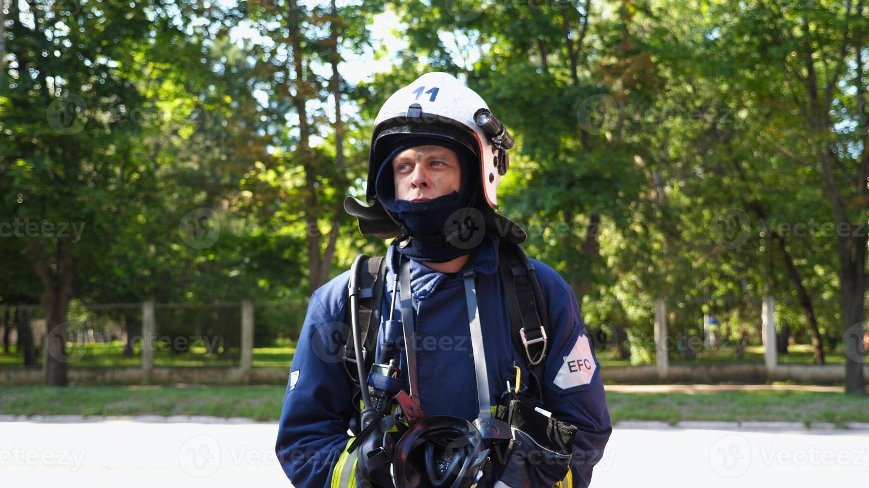 Portrait of tired male firefighter in protective uniform standing outdoor. Young fireman with dirty face posing after fire outside. Concept of saving lives and heroic profession. Slow motion photo