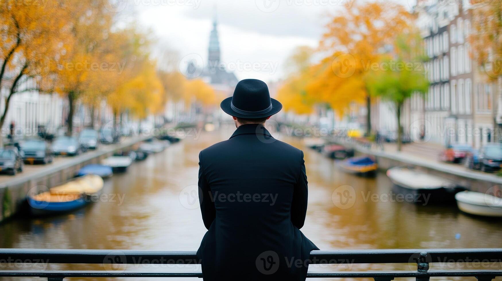 Man in black hat overlooking canal with autumn trees and boats. photo