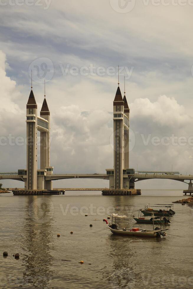 A stunning photogenic Kuala Terengganu drawbridge under a dramatic cloudy sky with structure featuring twin towers and a modern design that nestled against the ocean below. photo