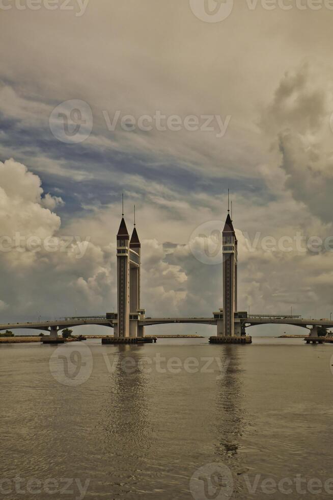 A stunning photogenic Kuala Terengganu drawbridge under a dramatic cloudy sky with structure featuring twin towers and a modern design that nestled against the ocean below. photo
