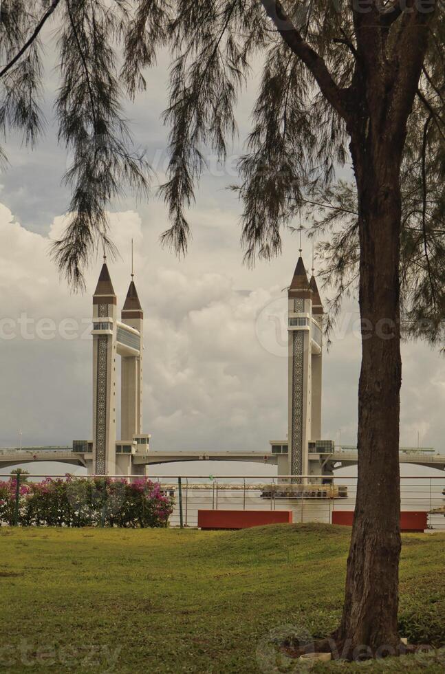 A stunning photogenic Kuala Terengganu drawbridge under a dramatic cloudy sky with structure featuring twin towers and a modern design that nestled against the ocean below. photo