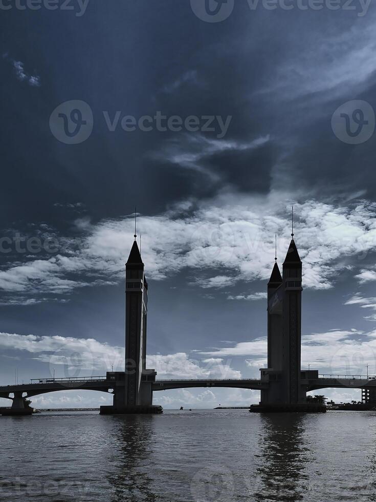 A stunning drawbridge looms against a moody sky with reflecting on rippling waters below. photo
