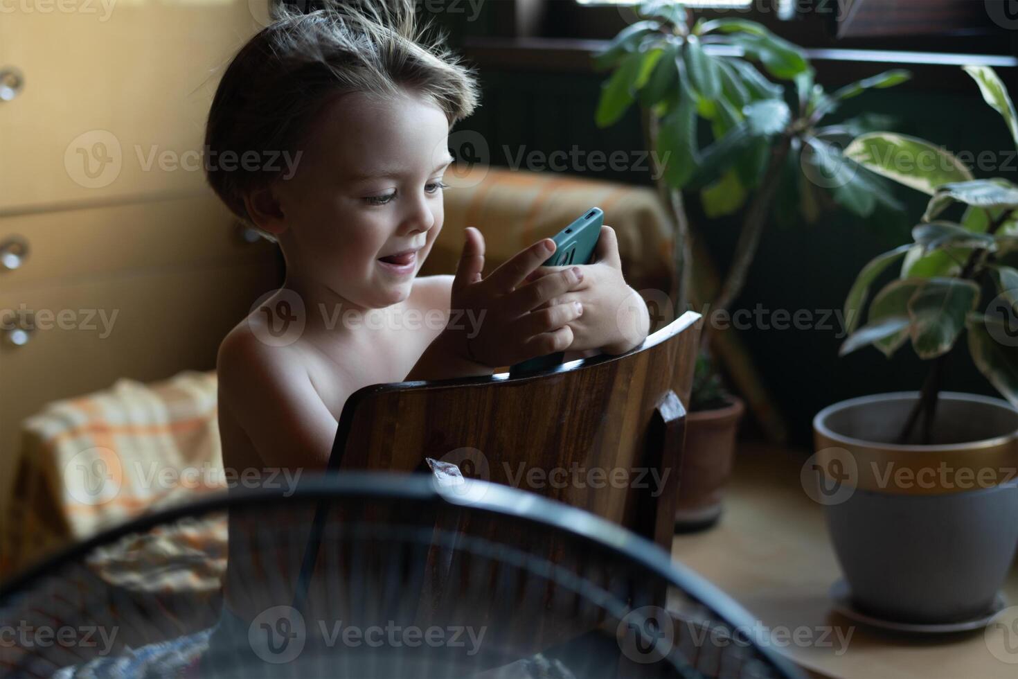 Cooling room, summer heat concept. Small child enjoying breeze from fan using smartphone at home. photo