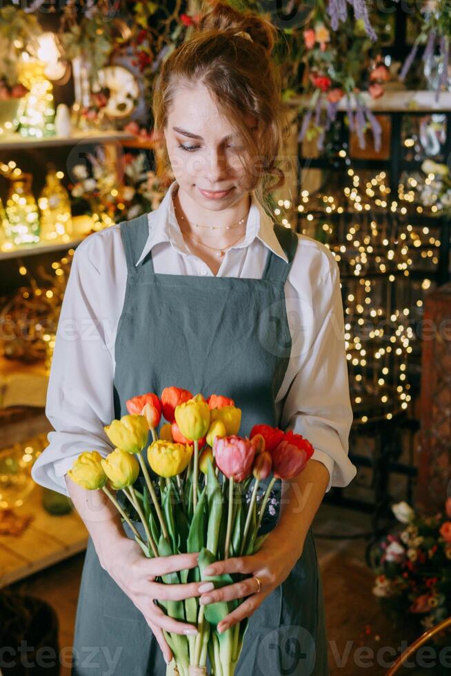 A woman in her florist shop collects bouquets of flowers. The concept of a small business. Bouquets of tulips for the holiday on March 8. photo