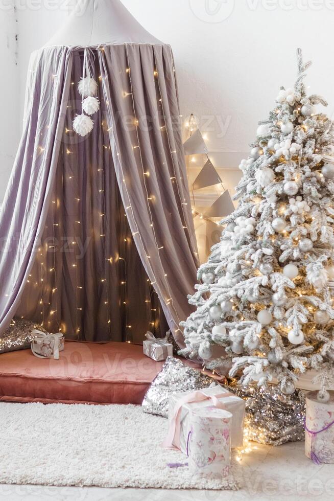 A Christmas tree sprinkled with artificial snow and a tent decorated with a luminous garland in the New Year's interior. Background for New Year wallpapers and postcards. photo