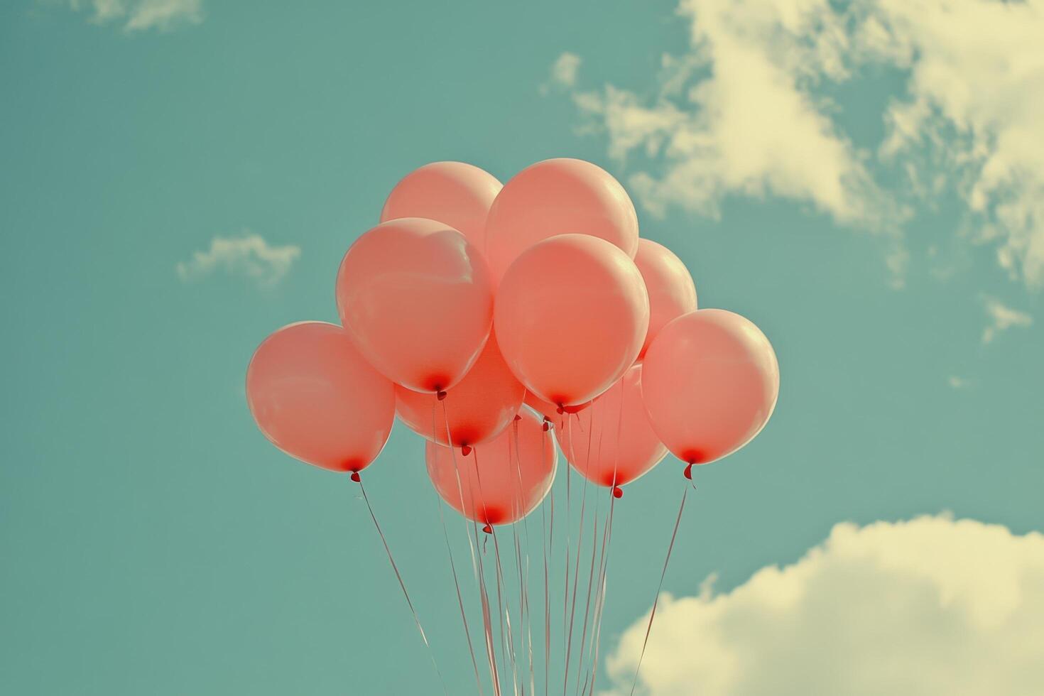 Pink balloons float against a bright blue sky with fluffy white clouds in a joyful outdoor setting photo