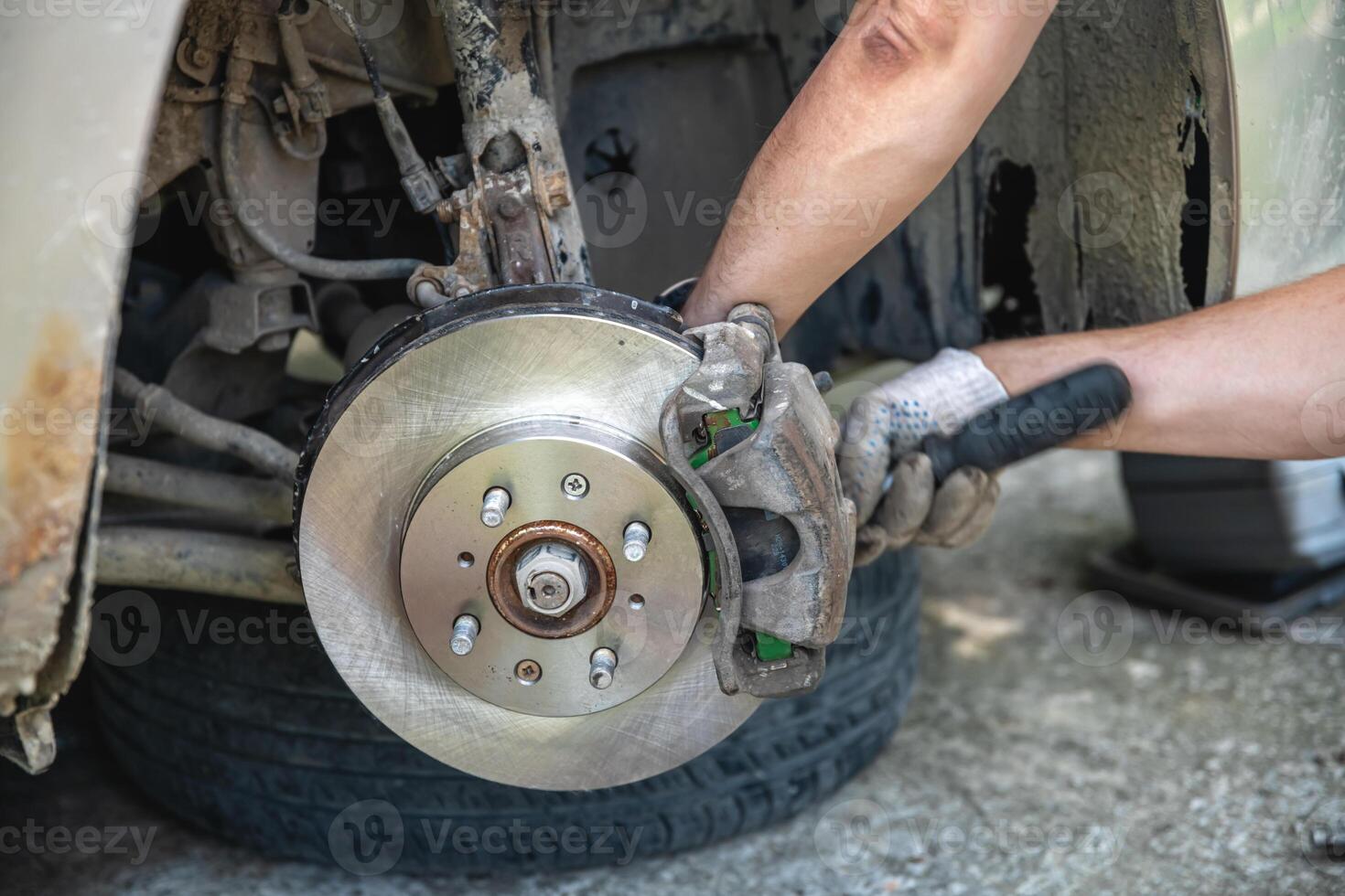 Mechanic man installing new brake disc and brake pads on car, car repair photo