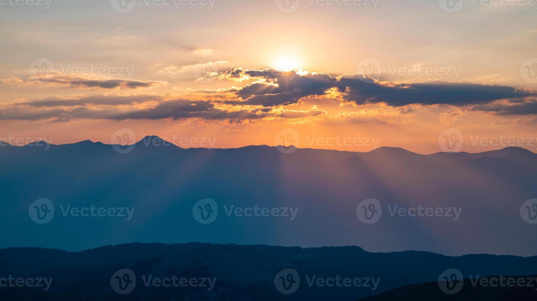 The setting sun over the mountains, the beautiful sun's rays shine through the clouds, the natural background, freedom, tranquility and peace photo