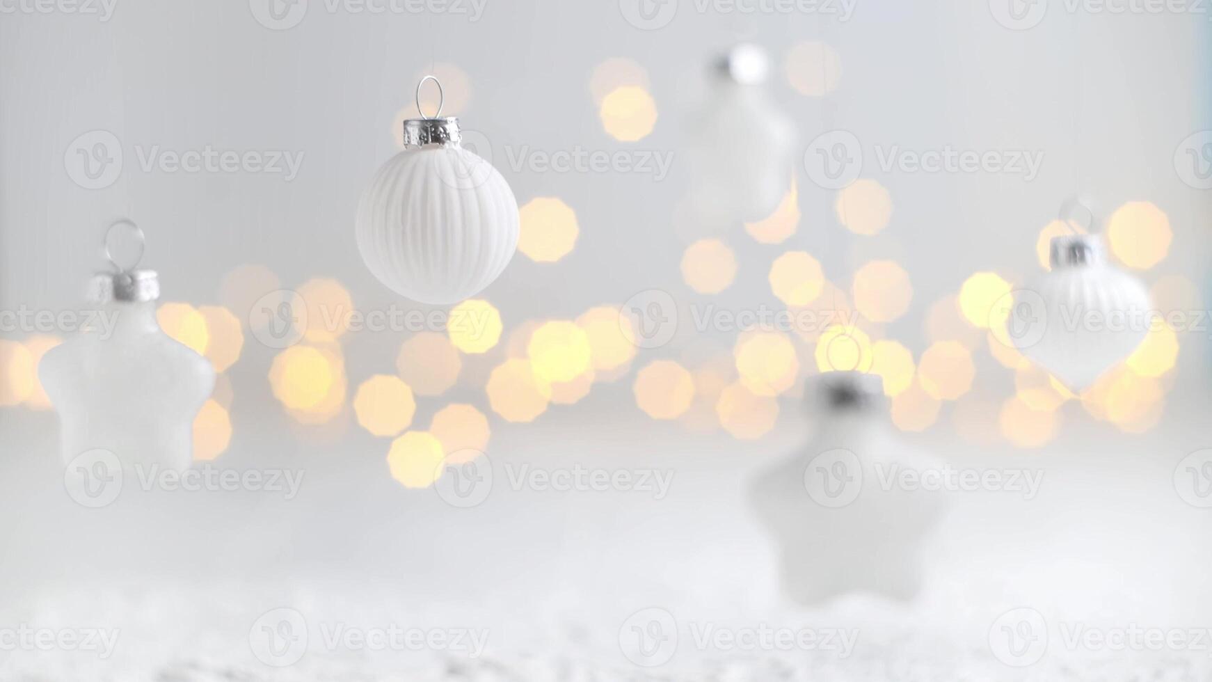 White christmas ornaments of various shapes hanging against a light background with soft, warm bokeh from sparkling lights, evoking a serene and festive holiday mood photo