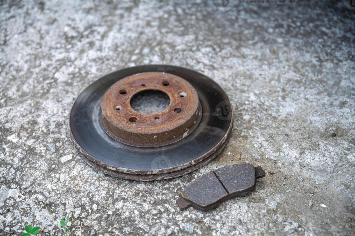 The old brake disc and brake pads are lying on a concrete surface, Repair of the car photo