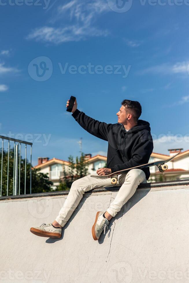 vertical Skater enjoying a fun selfie moment with smartphone at the half-pipe in skate park photo