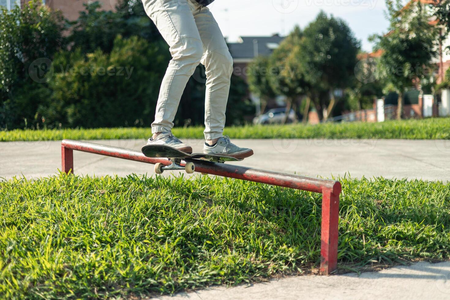 Low-angle close-up of skater's legs grinding a red rail at the skate park photo