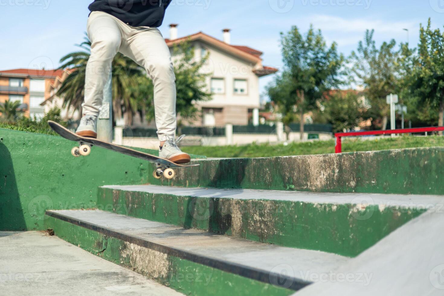 Close-up of an unrecognized skater jumping down green stairs at the skate park photo