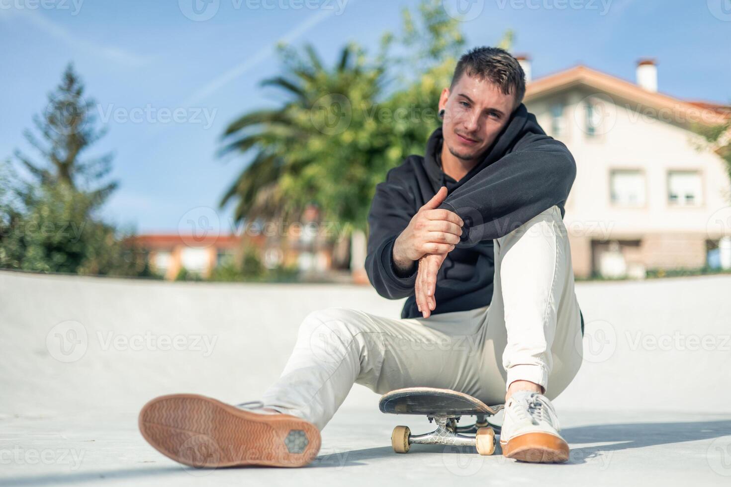 Casual skater smiling at the camera while sitting on their board in the skate park photo