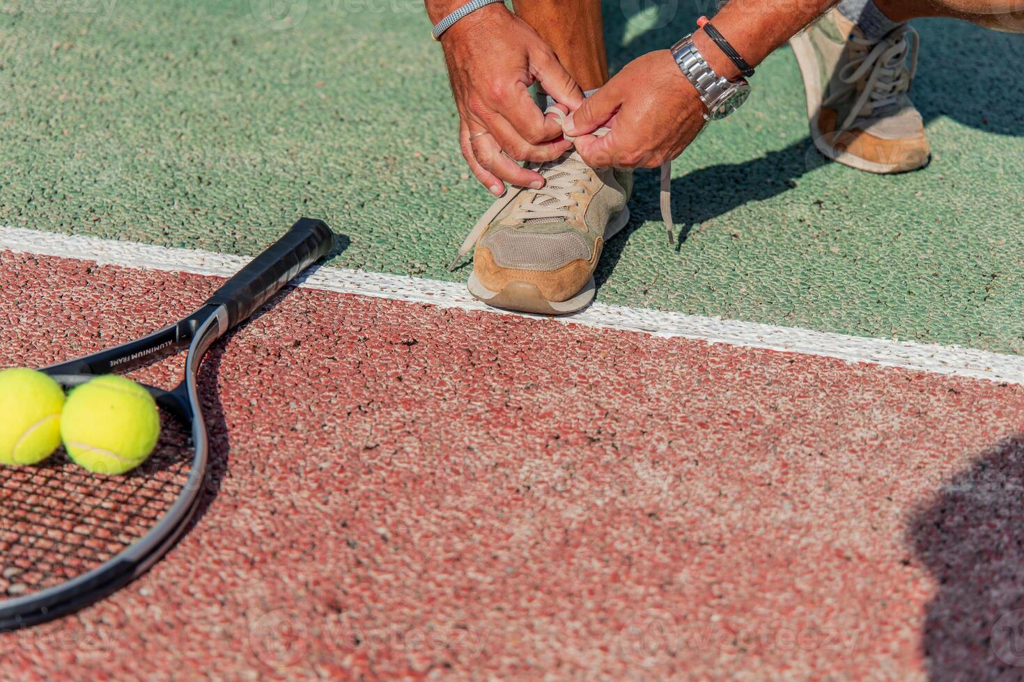 Close-up of man tying shoe with racket and tennis ball on court before match photo
