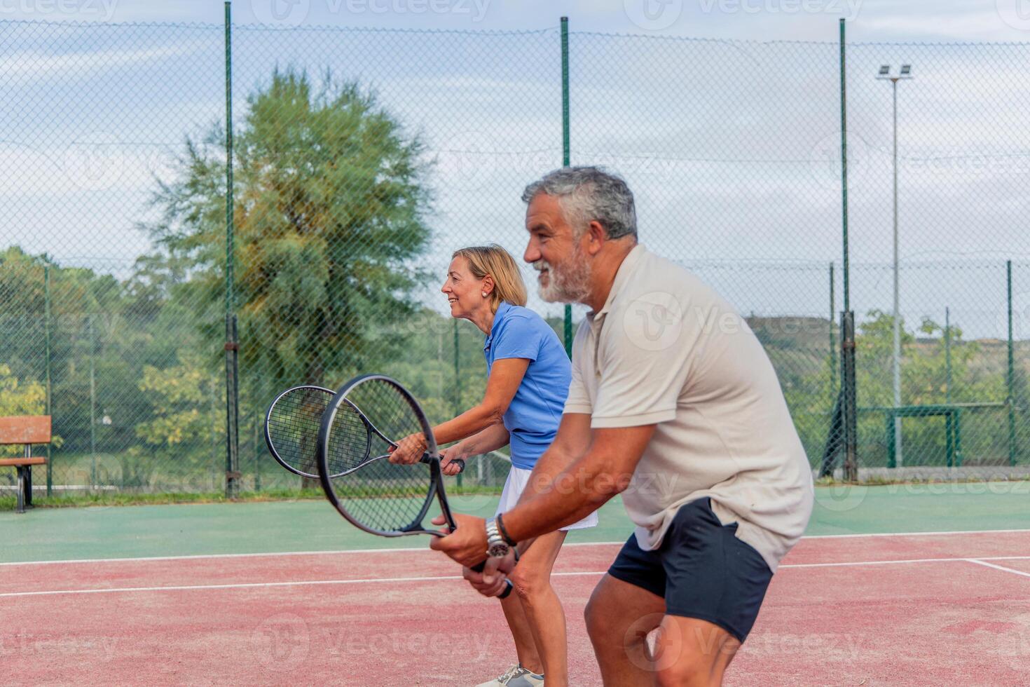 lateral view of senior tennis couple holding rackets ready to play during match photo