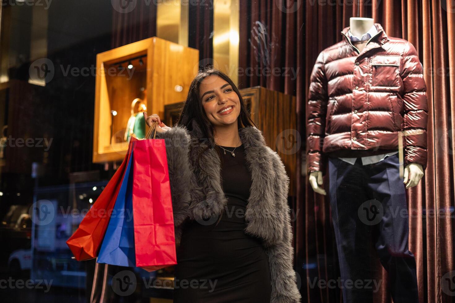 Low-angle shot of smiling young latina shopping through city stores at night photo