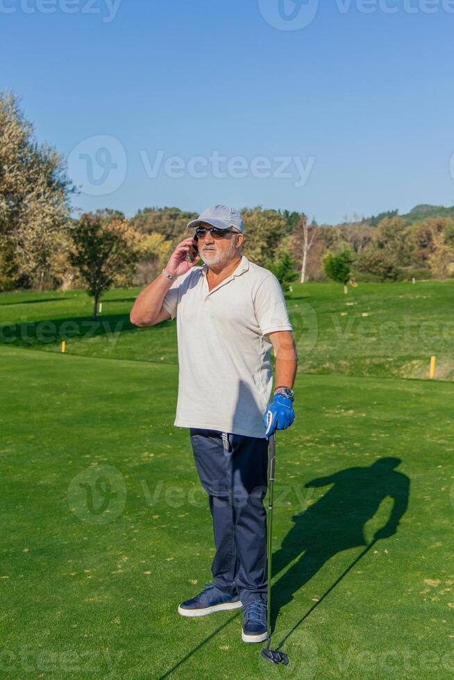 vertical senior golfer on business call with smartphone during golf match photo