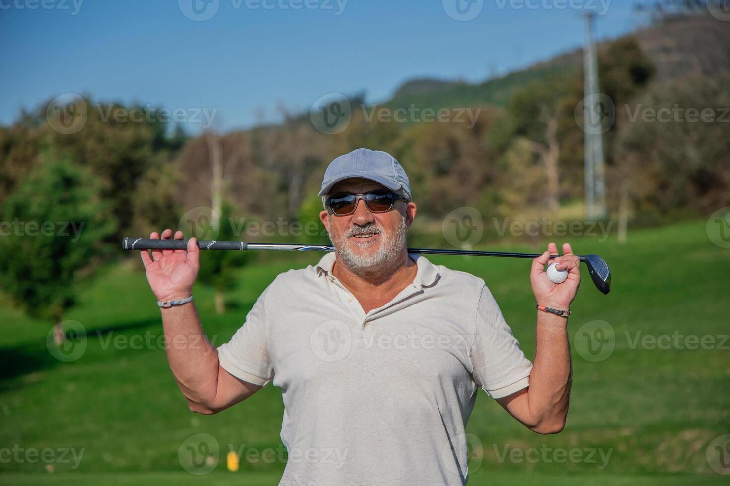 Elderly golfer with sunglasses and cap smiling with golf club on shoulders on the course photo