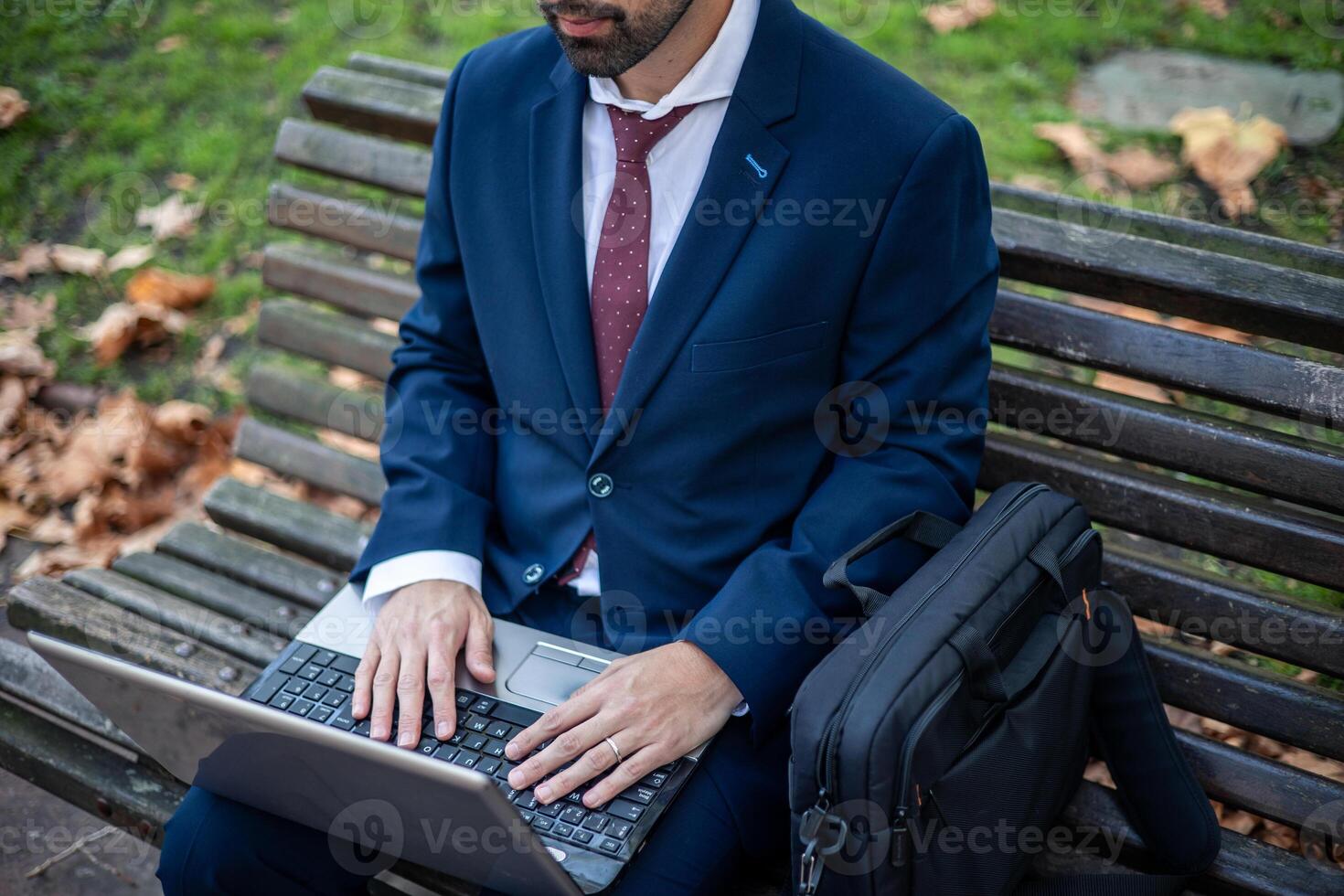 Unrecognizable businessman works with laptop sitting on a park bench outdoors photo