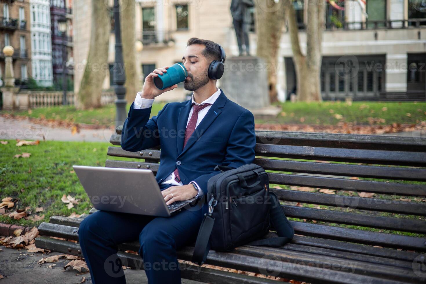 Relaxed businessman enjoys coffee while reviewing his business project on a laptop in the park photo